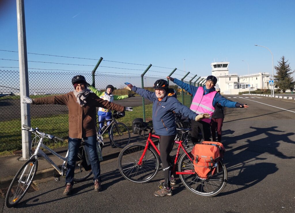 Quelques cyclistes mimant un avion avec les bras tendus devant l'aérodrome de Toussus le Noble
