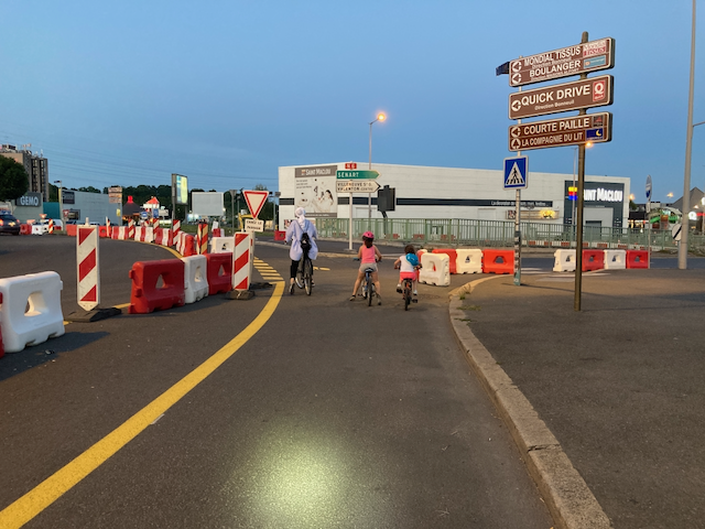 Une maman et ses deux enfants, chacun·e sur leurs vélos, vigilants sur l'anneau cyclable temporaire du carrefour Pompadour